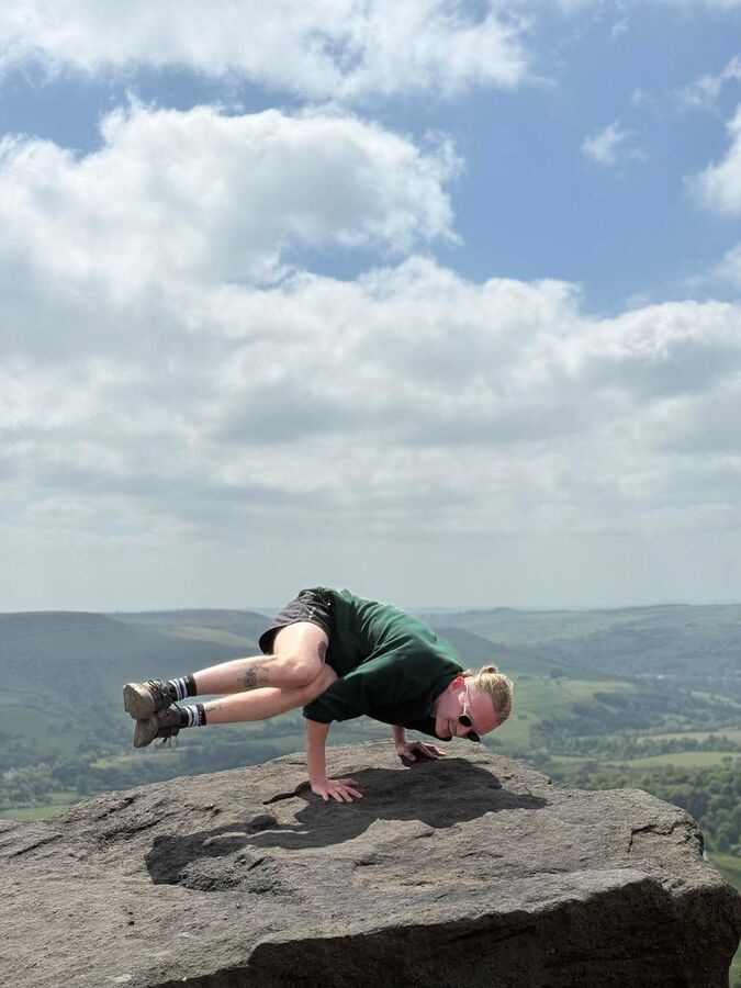 James balancing in crow pose on a rock overlooking the Peak District